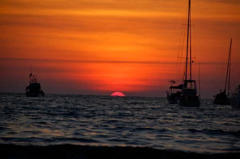 Red Sunset with sun in mid frame between two boats on the ocean Foto stock