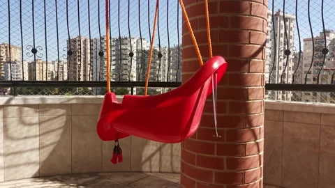 Red swing hanging from ceiling on balcony swaying with wind Stock Footage 213967168
