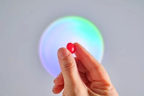 A red tablet of a vitamin complex in a hand. Stock Photos