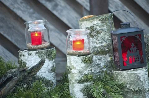 Red tea lights in glasses and in a lantern on wooden trunks with branches, 스톡 사진