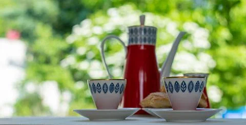 Red teapot with blue pattern teapot and two white cups on a wooden table facing Stock Photos