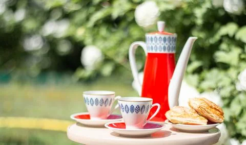 Red teapot with blue pattern teapot and two white cups on a wooden table facing Stock Photos