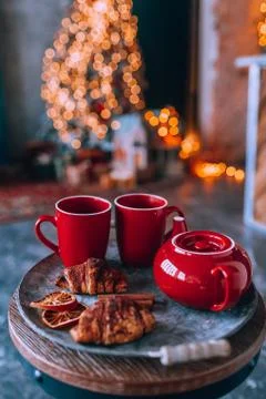 Red teapot with two red cups on a tray with dry orange and croissant. Lights  Stock Photos