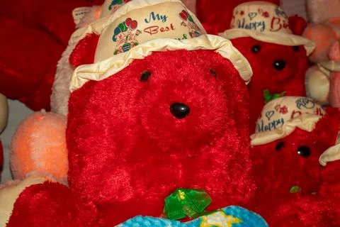 Red teddy bear wearing personalized hat sits among toy collection. Stock Photos
