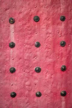 Red textured surface with rows of evenly spaced black rivets. Stock Photos