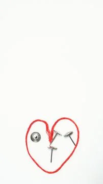 Red thread forms heart shape with metal fasteners and button on white backg.. Stock Photos