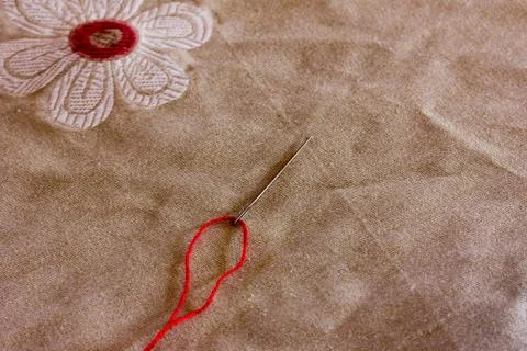 Red thread inserted into a needle on the background of linen fabric with a pa Foto stock