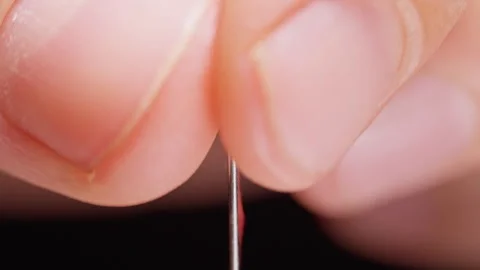 Red Thread Passes Through a Sewing Needle Eye on a Black Background, Detailed Ma Stockbeeldmateriaal 341417232