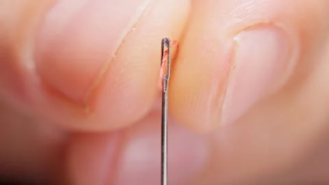 Red Thread Passes Through a Sewing Needle Eye, Extreme Macro View Against Black Stockbeeldmateriaal 341418046