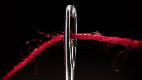 Red thread passing through eye of a needle sewing macro Stock Footage 340030665