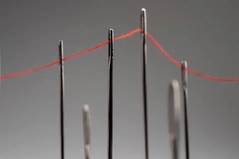 Red thread passing through needles on a grey background 스톡 사진