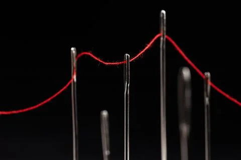 Red thread passing through needles on a black background Stock-Fotos