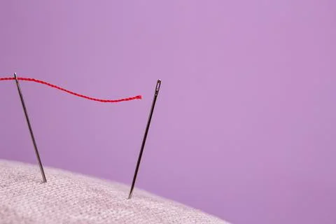 Red thread for sewing is threaded into the eye of the needle and directed to  Stock Photos