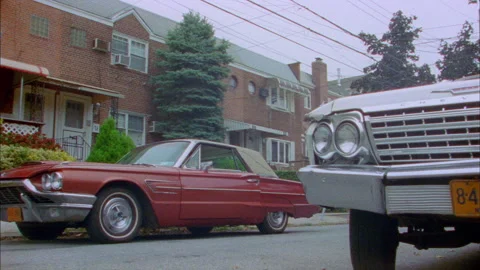 Red Thunderbird comes down street and a man gets out and walks down the street Stock Footage 272260081