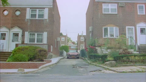 Red Thunderbird comes down street and a man gets out and walks down the street Stock Footage 272837577