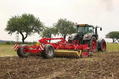 Red tilling tool in rape stubble attached to green tractor, preparing soil .. Stock Photos