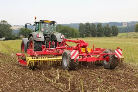 Red tilling tool in rape stubble attached to green tractor, preparing soil .. Stock Photos