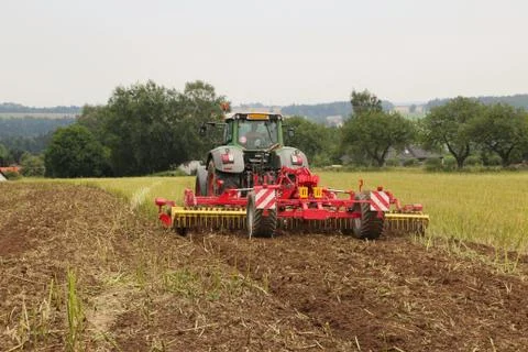 Red tilling tool in rape stubble attached to green tractor, preparing soil .. Stock Photos
