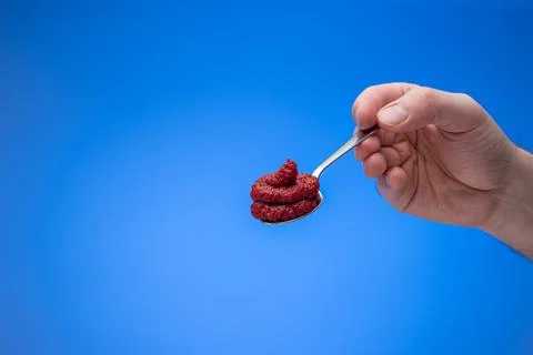Red tomato concentrate paste in a small spoon held in male hand. Close up stu Fotos de archivo