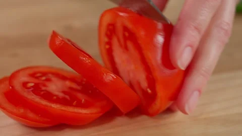Red tomato is cut into slices by the hands of a girl on a wooden board Stock Footage 253548601