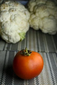 Red tomato placed on a a table mat with out focus cauliflowers in the backg.. Stock Photos