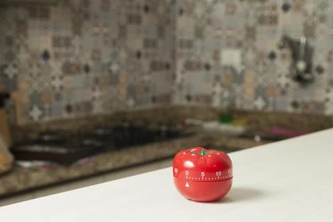 Red tomato-shaped kitchen timer with cooking in the background. To let you kn Stock Photos