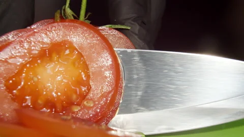 Red tomatoes are cut with a large chef's knife on a board, macro, water drops Stock Footage 134808126