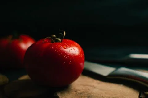 Red tomatoes on a black background, two steel knives are lying nearby Foto stock