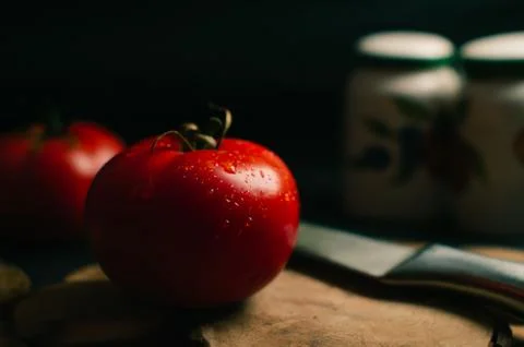 Red tomatoes on a black background, two steel knives and salts are lying nearby Stock Photos
