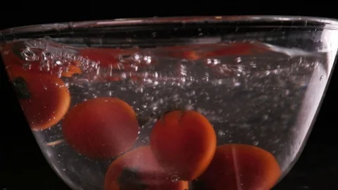 Red tomatoes fall and float in water, black background, slow motion 库存影片 108685664