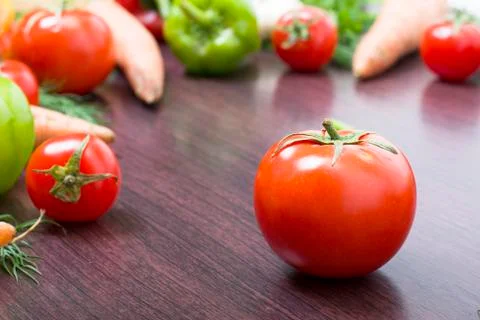 Red tomatoes on a table on a background of vegetables. Stock Photos