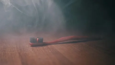 Red Toothbrush Lying in Drifting Smoke on Dark Wooden Surface Video stock 338998941