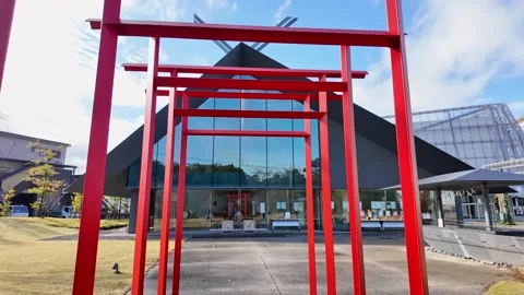 A red torii gate tunnel leads the viewer toward a modern glass building. Vídeos de archivo 346012080