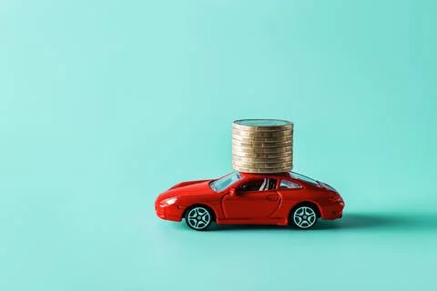 Red toy car carrying a stack of coins against blue background. Stock Photos