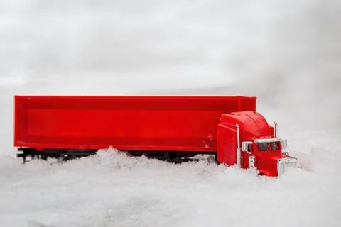 A red toy truck rides in the winter on a snowy road making its way through th Stock Photos