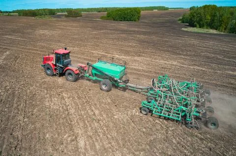 A red tractor is actively tilling a large, flat agricultural field Stock Photos