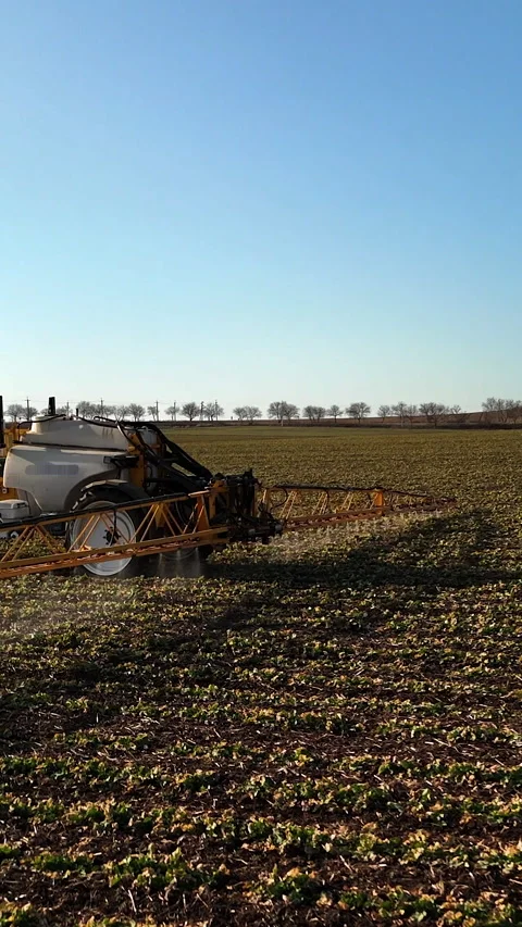 Red tractor with attached sprayer moves across agricultural field under clear 스톡 동영상 336948471