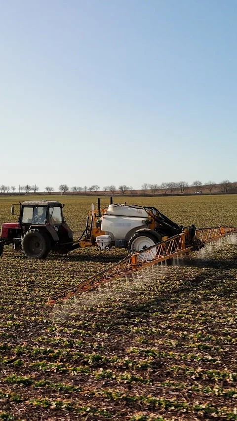Red tractor with attached sprayer moves across a vast agricultural field under a 库存影片 336948695