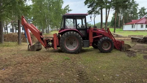 Red tractor with backhoe bucket parked on dirt near houses and trees Stock Footage 341510311