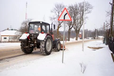 Red tractor clears the road from snow Stock Photos