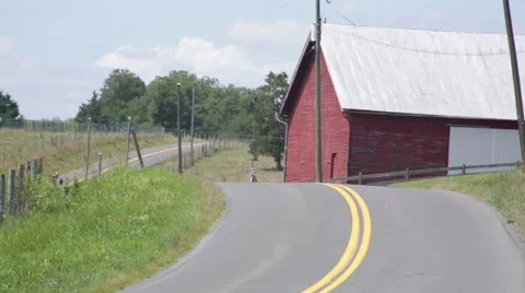 Red tractor driving down a windy country road Stock Footage 66501097