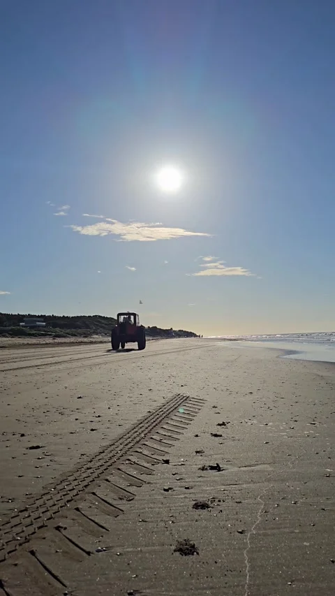 Red tractor driving on sandy beach under the bright sun Stock Footage 329485950