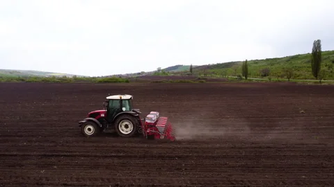 Red tractor equipped with a seed drill is plowing a large field, creating Stock Footage 325196930