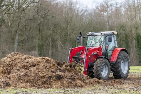 Red tractor with front loader in front of a manure heap Stock Photos