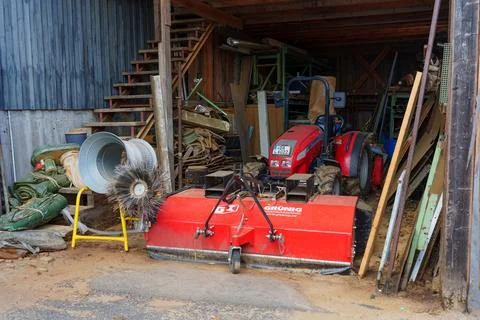 Red tractor with Grünig sweeper attachment inside a rustic barn 库存照片