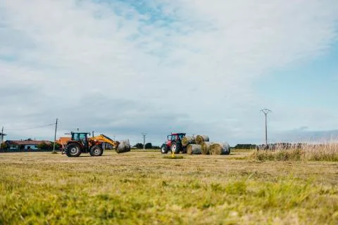 Red tractor loading a trailer with straw bales Stock Photos