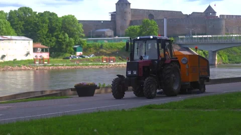 Red Tractor with Orange Street Sweeper Driving on Riverside Embankment Stock Footage 337880111