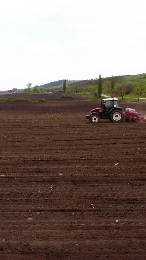 Red tractor plowing a brown field, creating furrows in the soil while dust rises Stock Footage 325201725