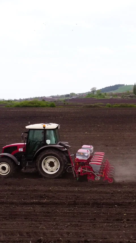 Red tractor plowing a field with a seed drill, showcasing the continuous action Stock Footage 325481664