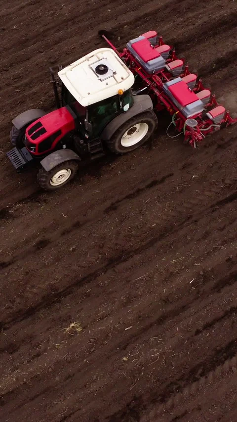 Red tractor plowing soil in a field, followed by a seed drill, showcasing the Stock Footage 325481724